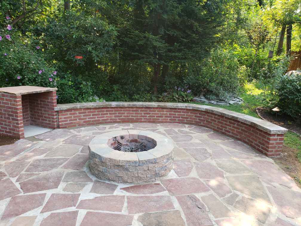 brick firepit and storage area with a brick wall and walkway around the red stone and sand ground