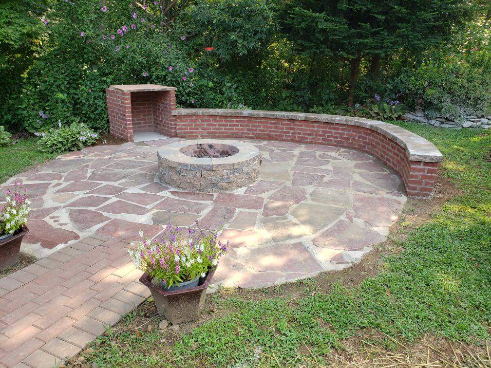 brick firepit and storage area with a brick wall and walkway around the red stone and sand ground