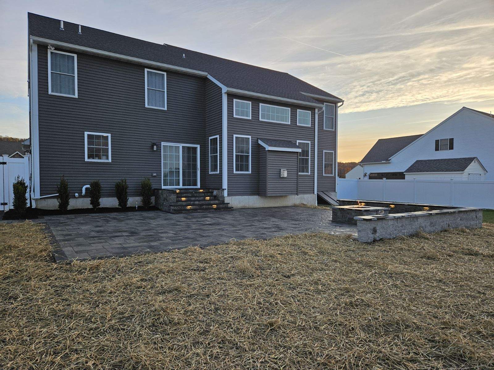 brand new patio spanning the width of the house with a firepit and steps up to a back door